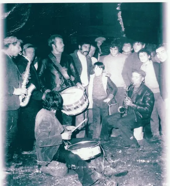 Música na rua à noite: saxofones e bombo, com gente à roda