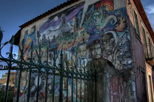 Parede pintada com um mural de cores, ao lado de um portão de ferro
