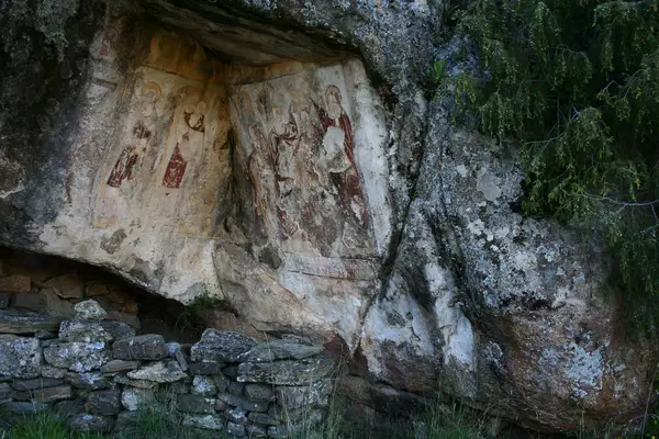 Pinturas num abrigo de rocha, com um muro de pedra à frente