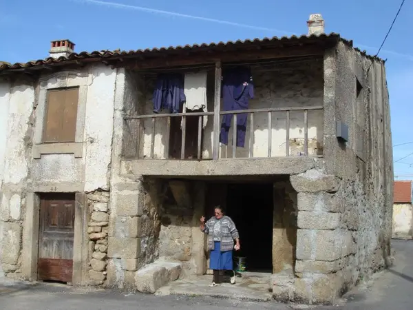 Casa de pedra com varanda de madeira, e uma mulher à porta