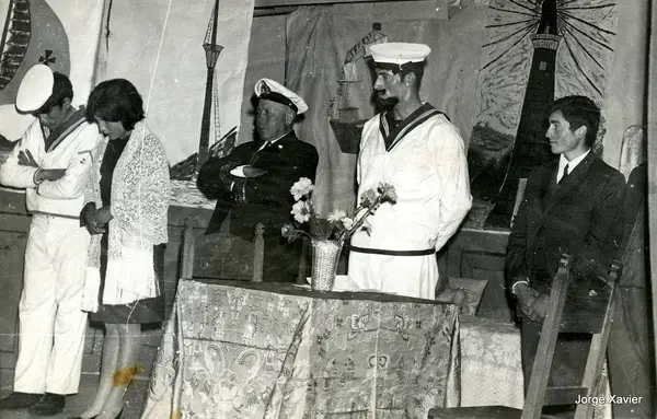 Cena de teatro: marinheiros e uma mulher num palco com cenário pintado