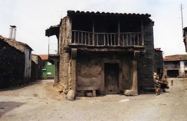Casa de pedra de dois pisos com varanda de madeira, numa rua de terra