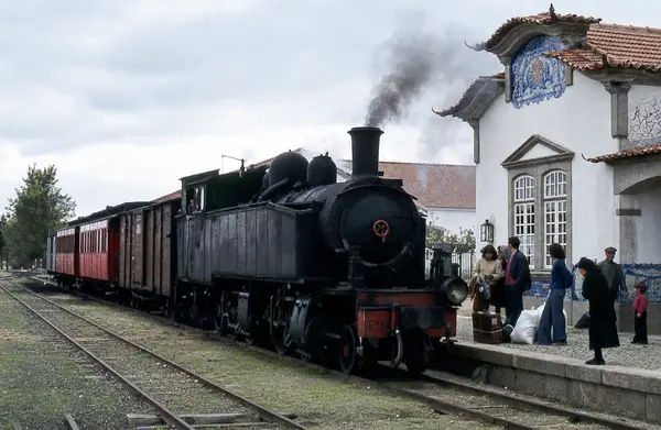 Locomotiva a vapor parada na estação, com gente na gare