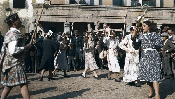 Festa na rua: gente de traje com varas e pandeiretas