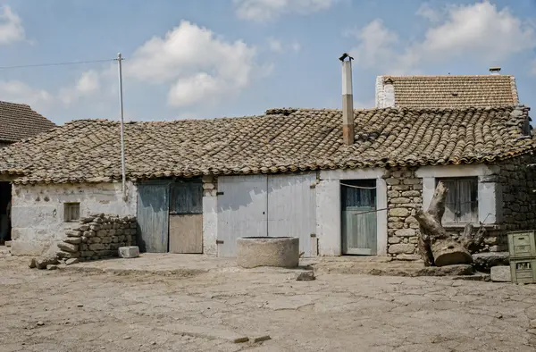 Casa baixa de pedra com telhado de telha, e um poço à frente