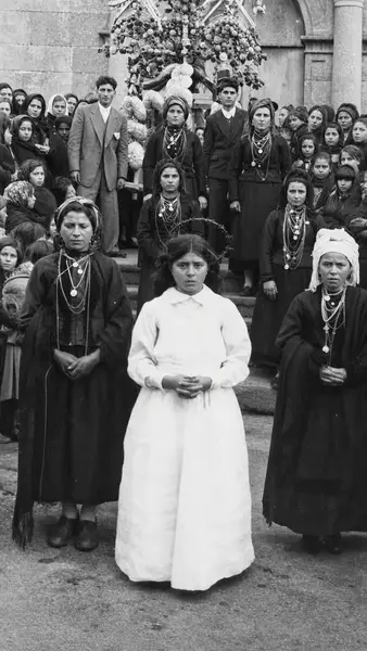 Três mulheres de traje à frente de um grupo, à porta da igreja